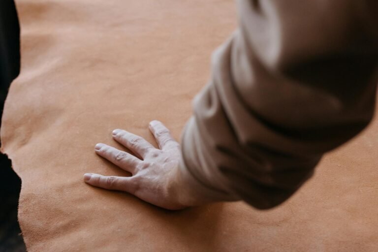 A hand gently resting on a piece of smooth brown leather, showcasing texture.