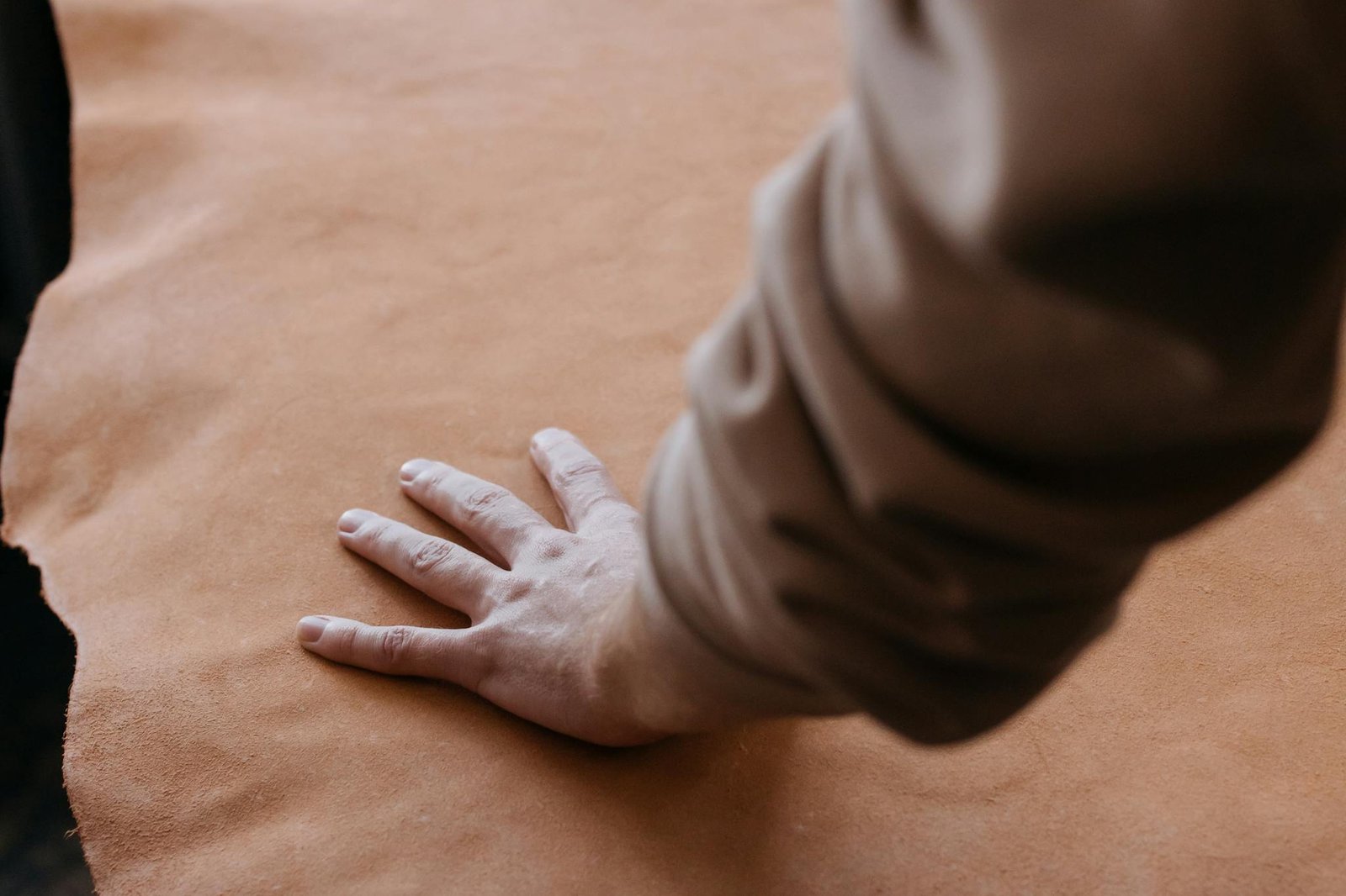 A hand gently resting on a piece of smooth brown leather, showcasing texture.