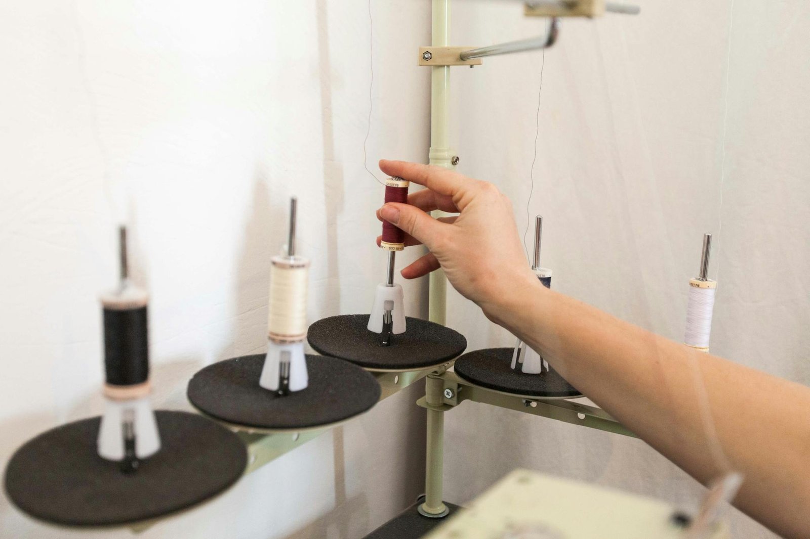 Close-up of a hand adjusting thread spools on an industrial sewing machine.