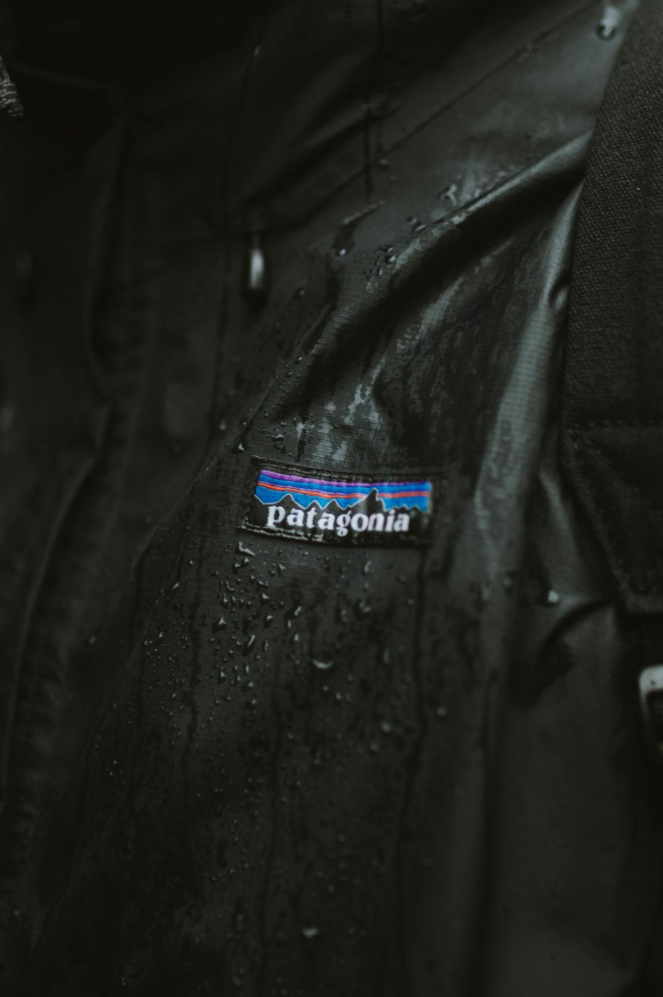 Detailed close-up of a black jacket with visible logo and water droplets, emphasizing texture and mood.